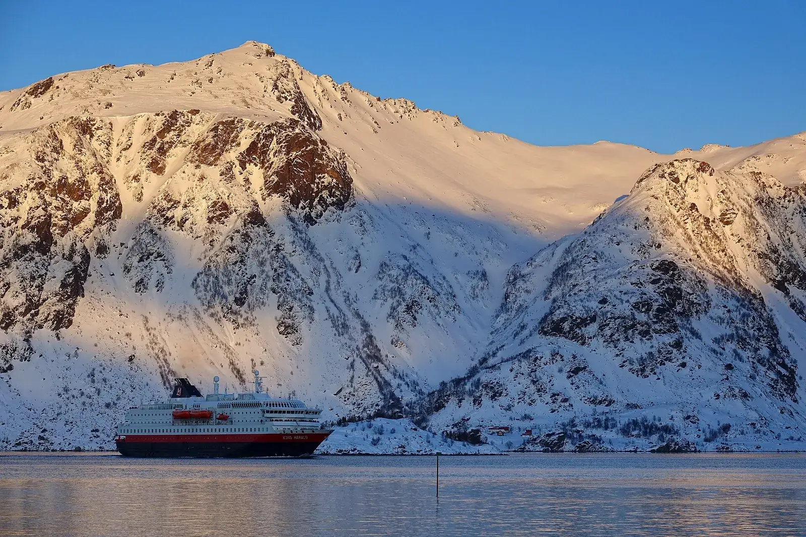 Hurtigruten coastal ship sailing below snow-covered mountains in northern Norway in winter