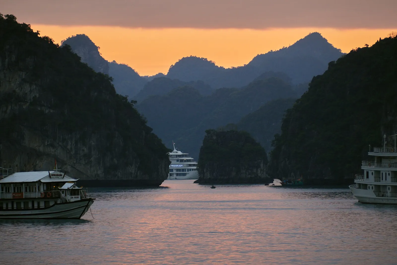 Limestone karst islands and overnight cruise boats at dusk in Ha Long Bay, Vietnam