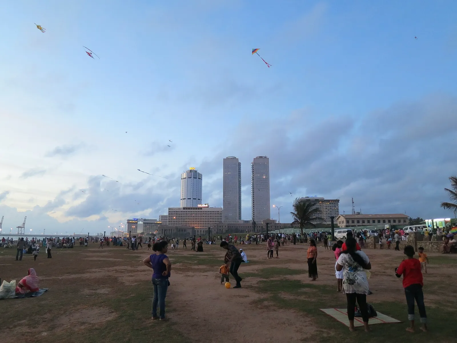 Families flying kites on Galle Face Green by the sea in Colombo, with city towers behind